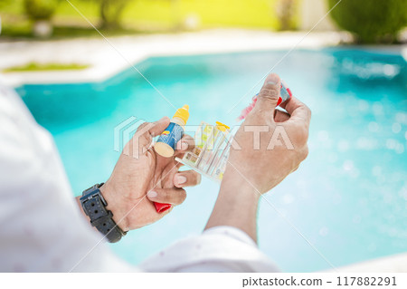 Hand holding a pool ph and chlorine tester, Hand holding Water Test Kit on blurred pool background, Person holding complete water test kit with blurred pool background Hand holding a pool ph and chlorine tester, Hand holding Water Test Kit on blurred pool background, Person holding complete water test kit with blurred pool background 117882291