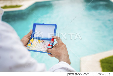 Hand holding Water Test Kit on blurred pool background, Hand holding a pool ph and chlorine tester, Person holding complete water test kit with blurred pool background Hand holding Water Test Kit on blurred pool background, Hand holding a pool ph and chlorine tester, Person holding complete water test kit with blurred pool background 117882293