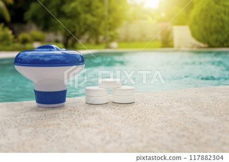 Tablets with chlorine dispenser for swimming pools. Chlorine tablets with dosing float, Pool float and chlorine tablets, A pool float and chlorine tablets on the edge of a swimming pool. 117882304
