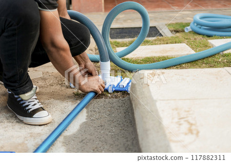 Pool suction hose installation. Person connecting pool hose handle. Man connecting the handle on the pool vacuum. Suction equipment connection for swimming pool 117882311