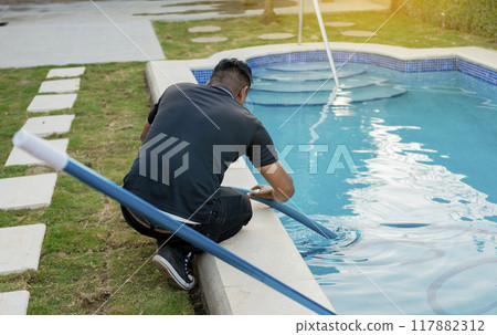 Maintenance person cleaning swimming pool with suction hose. Cleaning and maintenance of swimming pools with suction hose. Crouched man cleaning swimming pool with vacuum hose Maintenance person cleaning swimming pool with suction hose. Cleaning and maintenance of swimming pools with suction hose. Crouched man cleaning swimming pool with vacuum hose 117882312