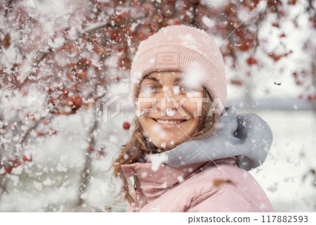 Winter Elegance: Portrait of a Beautiful Girl in a Snowy European Village. Winter lifestyle portrait of cheerful pretty girl. Smiling and having fun in the snow park. Snowflakes falling down 117882593