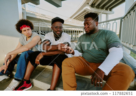 Biracial guys sharing lit cigarette while communication on stairs 117882651