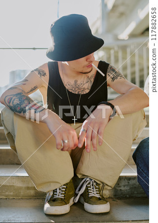 Unrecognizable man sitting on stairs and holding cigarette in mouth 117882658