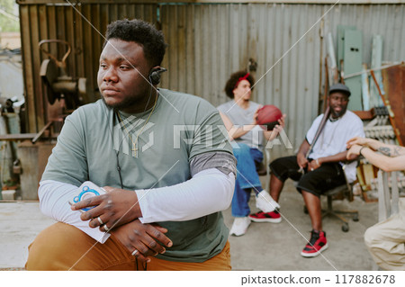 Man holding music player and enjoying music while his friends sitting in old chairs and chatting 117882678