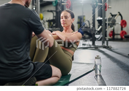 Male unrecognizable coach holding brunettes legs while she swinging abdominal muscles Male unrecognizable coach holding brunettes legs while she swinging abdominal muscles 117882726