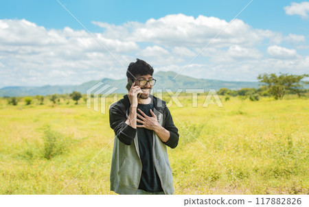 Smiling man calling on the phone on the field, people talking on the cell phone in the field. Man calling on the phone in the field, A man in a beautiful field talking on the phone Smiling man calling on the phone on the field, people talking on the cell phone in the field. Man calling on the phone in the field, A man in a beautiful field talking on the phone 117882826
