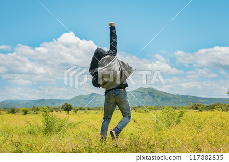 Man from back jumping in a nice field, Rear view of man jumping in the grass raising fist, Concept of a free person jumping and raising his arm, Free person jumping from back in the field 117882835