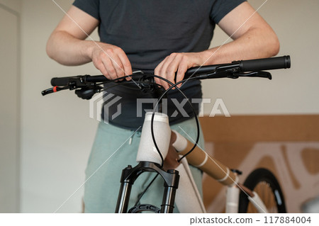 A man is inside working on assembling bike handlebars as part of his bicycle maintenance task. Delivering goods from marketplaces A man is inside working on assembling bike handlebars as part of his bicycle maintenance task. Delivering goods from marketplaces 117884004