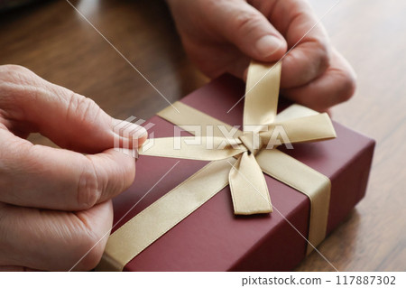 Hands of an elderly woman undoing the ribbon on a gift 117887302