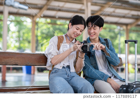 Happy Asian couple holding suitcases and camera preparing to wait for train at train station for vacation trip together. Happy Asian couple holding suitcases and camera preparing to wait for train at train station for vacation trip together. 117889117