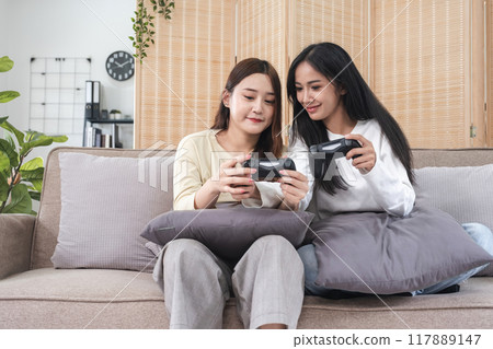 Young LGBT woman, lesbian couple, sitting on the sofa, playing games on a joystick together, having fun. 117889147