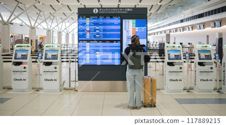 Young Asian woman in international airport looking at flight information board, checking her flight 117889215