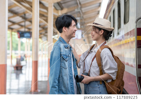 Happy Asian couple holding suitcases and camera preparing to wait for train at train station for vacation trip together. 117889225