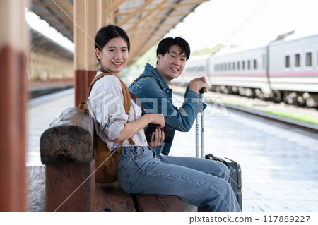 A young Asian couple waits for their train together at the train station, waiting to travel. 117889227