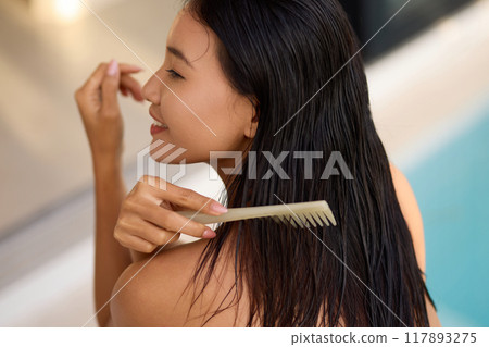 Woman Combing Wet Hair by Poolside Relaxing and Smiling in Natural Light Woman Combing Wet Hair by Poolside Relaxing and Smiling in Natural Light 117893275