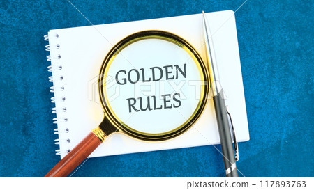 Conceptual golden rule symbol. Copy space. GOLDEN RULES words through the lens of a magnifying glass in a notebook and an abstract background 117893763