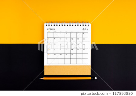 Top view of July 2025 desk calendar and pencil on yellow and black background. 117893880
