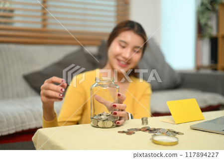 Cheerful young woman counting and stacking coins on a table. Saving money and financial responsibility concept 117894227