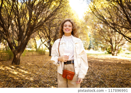 Smiling young woman with the photo camera walking in the park Smiling young woman with the photo camera walking in the park 117896991