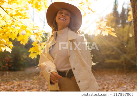 Smiling young woman enjoys the autumn weather in the forest with the yellow leaves at evening time Smiling young woman enjoys the autumn weather in the forest with the yellow leaves at evening time 117897005