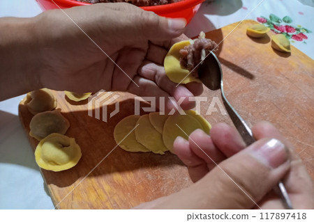 Process of modeling dumplings by hand, piece of minced meat is placed on dough blank with one hand with metal spoon for further wrapping. Kitchen work for preparation of homemade national food Process of modeling dumplings by hand, piece of minced meat is placed on dough blank with one hand with metal spoon for further wrapping. Kitchen work for preparation of homemade national food 117897418
