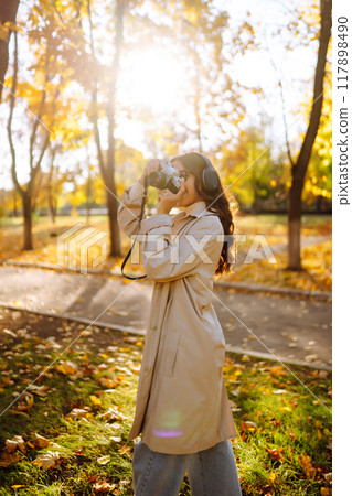 Beautiful woman taking pictures in autumn forest. Woman enjoying autumn weather. Lifestyle concept. 117898490