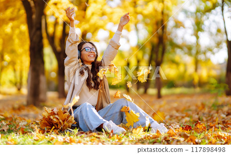 Young woman smiling and throwing maple leaves up in the air. 117898498