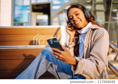 Young woman in headphones with a laptop on a city street. ?nline training. Freelancer. 117898688