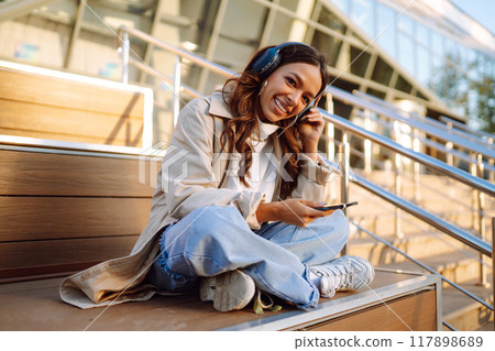 Young woman in headphones with a laptop on a city street. ?nline training. Freelancer. 117898689