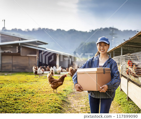 Stock image of a smiling woman holding a cardboard box at a chicken farm 117899090