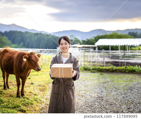 Stock image of a smiling woman holding a cardboard box at a dairy farm 117899095