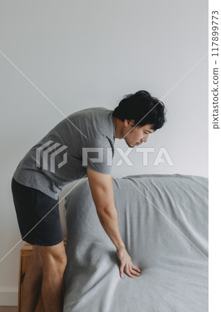 Man is doing his house work, covering the sofa with grey sheet. Man is doing his house work, covering the sofa with grey sheet. 117899773
