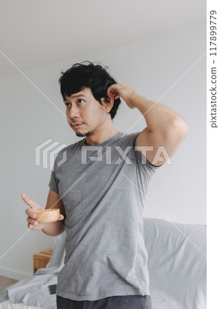 Man scratching his head, standing in the room and holding a cup of peanuts. Man scratching his head, standing in the room and holding a cup of peanuts. 117899779