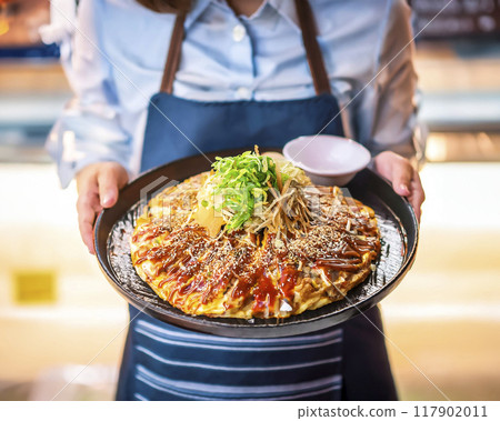 Image of a female store clerk carrying freshly made okonomiyaki 117902011