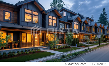 A row of beautiful townhouses with modern dark gray and wood accents, featuring large windows that glow warmly from the inside 117902093