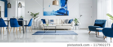 White living room with blue chairs, sofa, and coffee table near a kitchenette with white walls, grey floor tiles 117902273