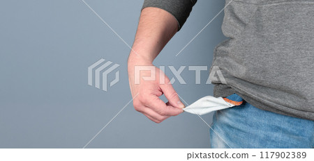 Young man in blue jeans and hoodie showing empty pockets on grey studio background. Millennial guy losing money, facing bankruptcy or unemployment during financial crisis. Economic depression concept 117902389