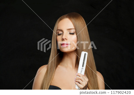 Nice smiling woman with long straight healthy hairstyle using straightening iron Nice smiling woman with long straight healthy hairstyle using straightening iron 117902420