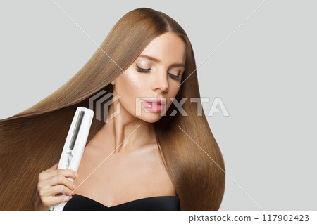 Glamorous fashion model woman using hair straighteners iron on white background.  117902423