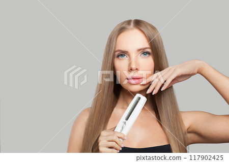 Nice fashion model woman using hair straighteners iron on white background. 117902425