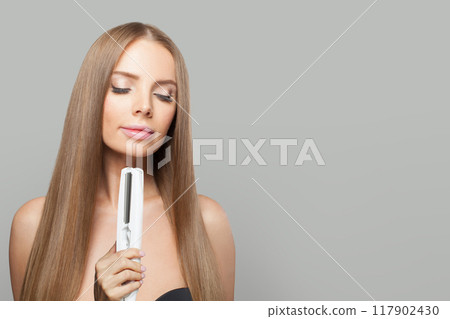 Brown-haired fashion model woman using hair straighteners iron on white background.  117902430