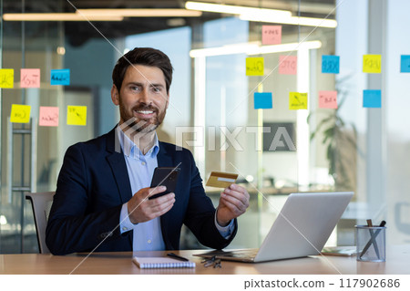 Businessman holding credit card and smartphone in office, exploring online payment and e-commerce. Man in suit demonstrating modern business environment with focus on digital finance solutions Businessman holding credit card and smartphone in office, exploring online payment and e-commerce. Man in suit demonstrating modern business environment with focus on digital finance solutions 117902686
