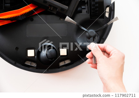 Maintenance of a smart robot vacuum cleaner. Women's hands maintain and clean a round robot vacuum cleaner. Organization of uninterrupted operation of a home cleaner 117902711