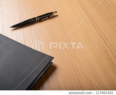 Notebooks and pens placed in a cluttered manner on a desk 117903162