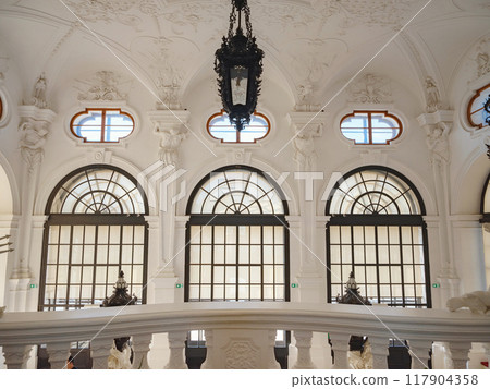 Wien, Austria - July 28, 2023: Impressive interior of hall in Upper Belvedere Palace in Vienna with staircase decorated with white stucco reliefs, sculptures and antique forged lanterns 117904358