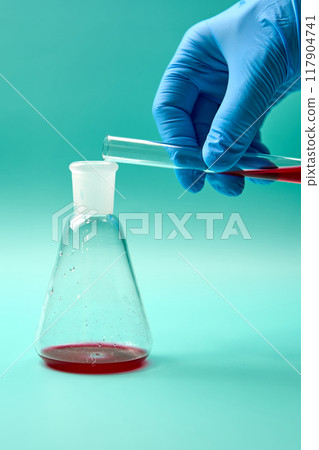 Scientist pouring red liquid into conical flask during experiment 117904741