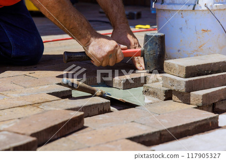 In course of reconstructing footpath, an employee is engaged in repairing damaged bricks In course of reconstructing footpath, an employee is engaged in repairing damaged bricks 117905327