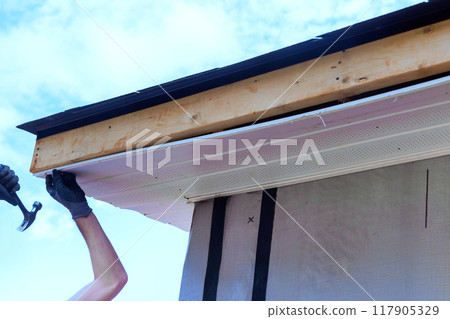 Worker installs plastic vinyl soffit on roof corner of rafters house 117905329