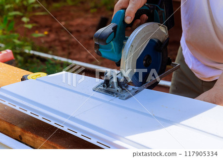 In process of construction, craftsman cuts vinyl siding panels to desired size before installing them In process of construction, craftsman cuts vinyl siding panels to desired size before installing them 117905334